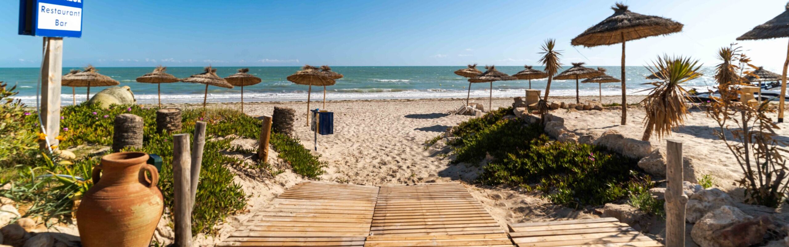 Panneau de l'hôtel au bord d'une allée en bois menant à la plage
