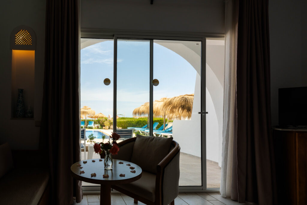 Salon de chambre avec porte-fenêtre ouvrant sur la piscine et les parasols de plage