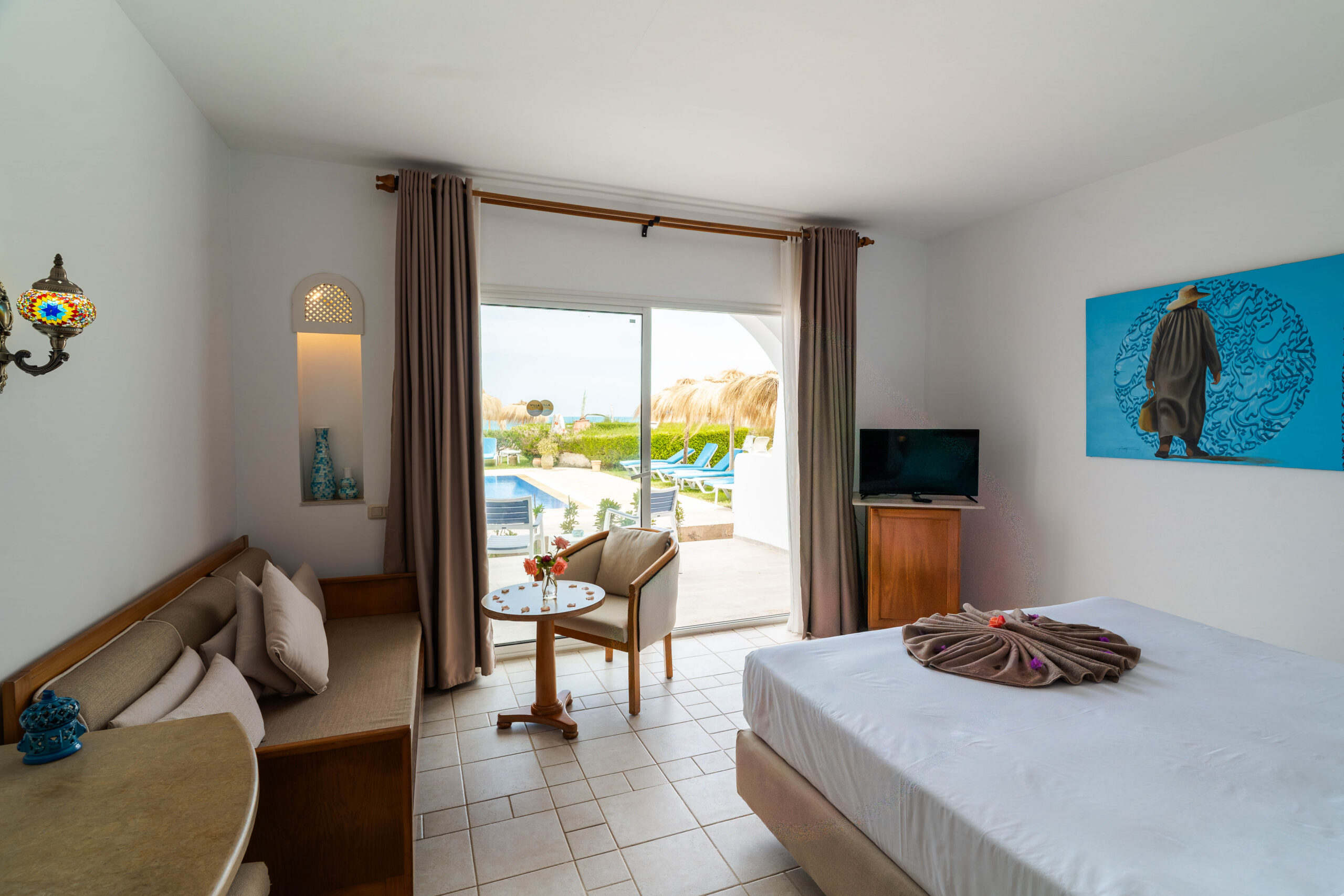 Chambre avec canapé, télévision et porte-fenêtre ouvrant sur la piscine
