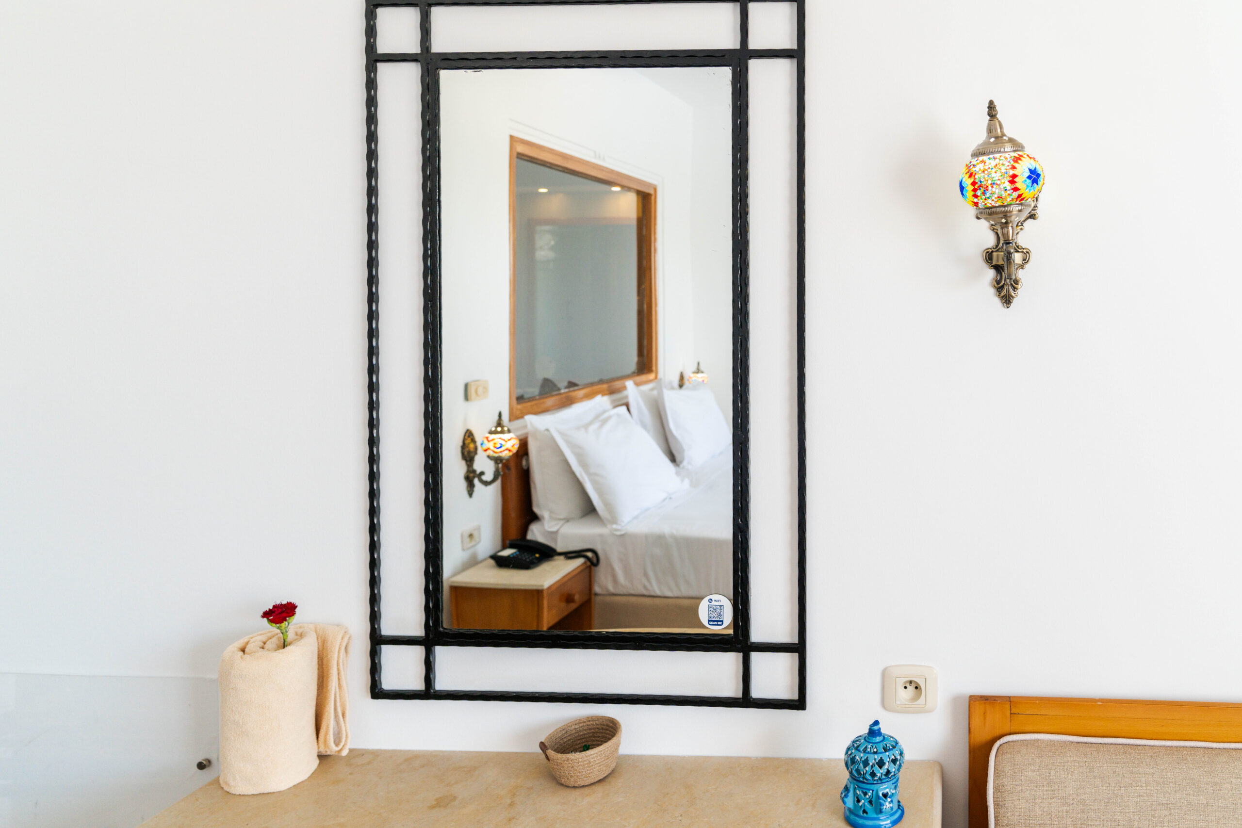 Miroir mural reflétant un lit avec objets décoratifs tunisiens sur la commode