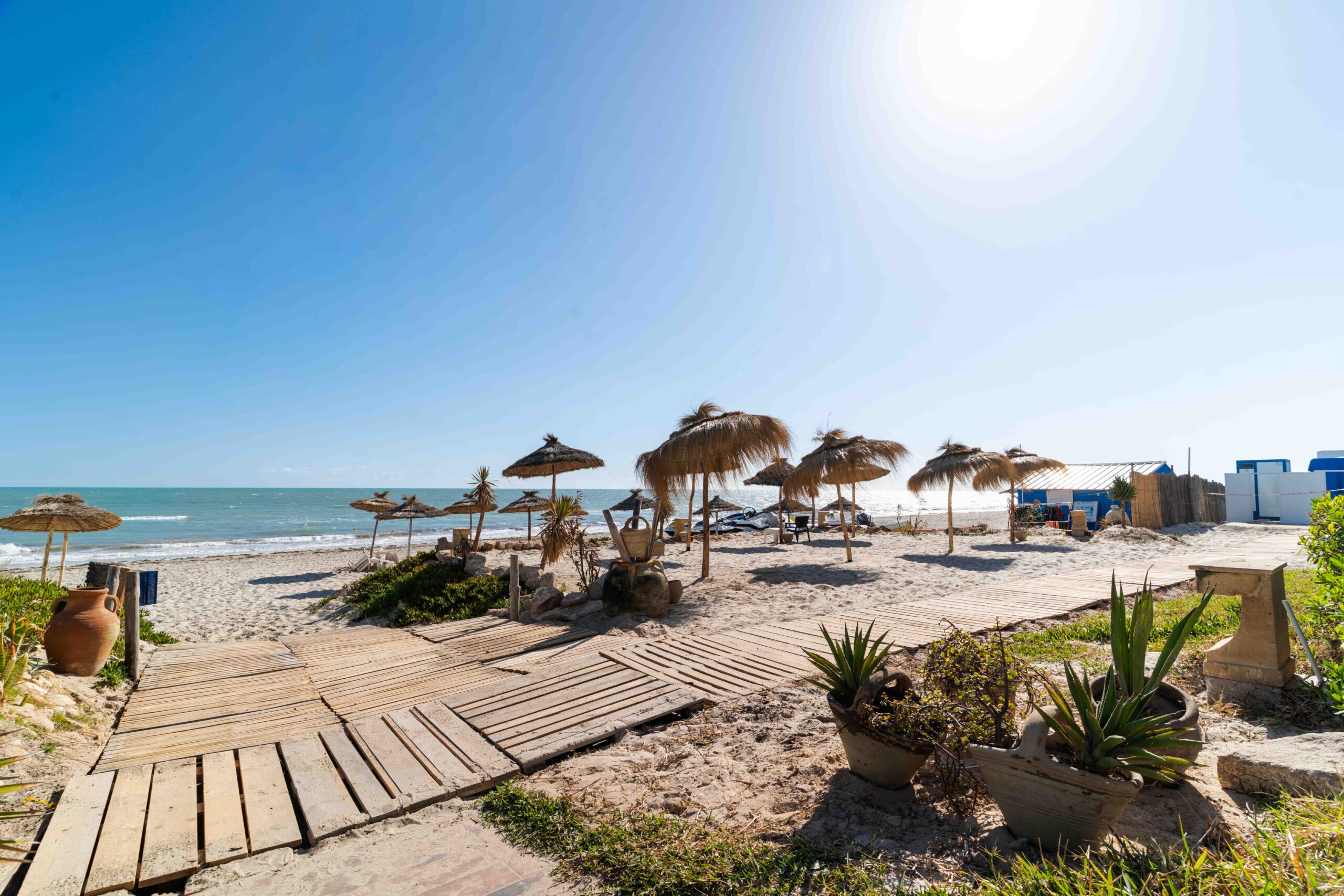 Ponton en bois traversant la plage vers des parasols en paille
