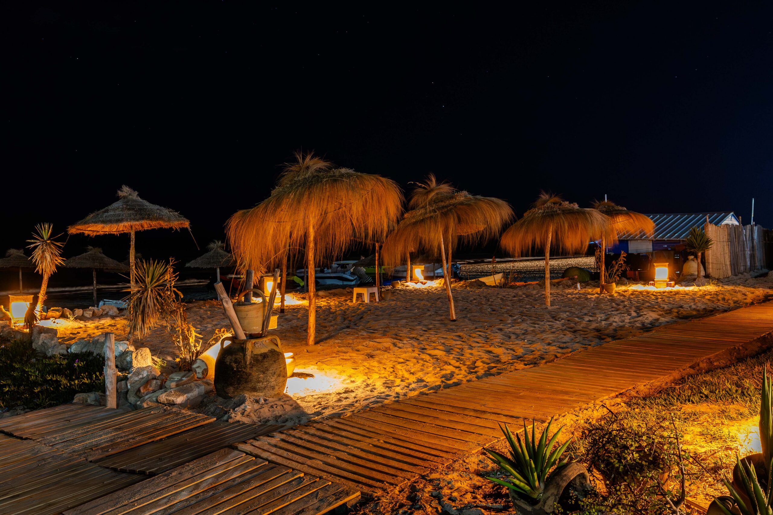 Allée en bois éclairée menant à des parasols de plage la nuit