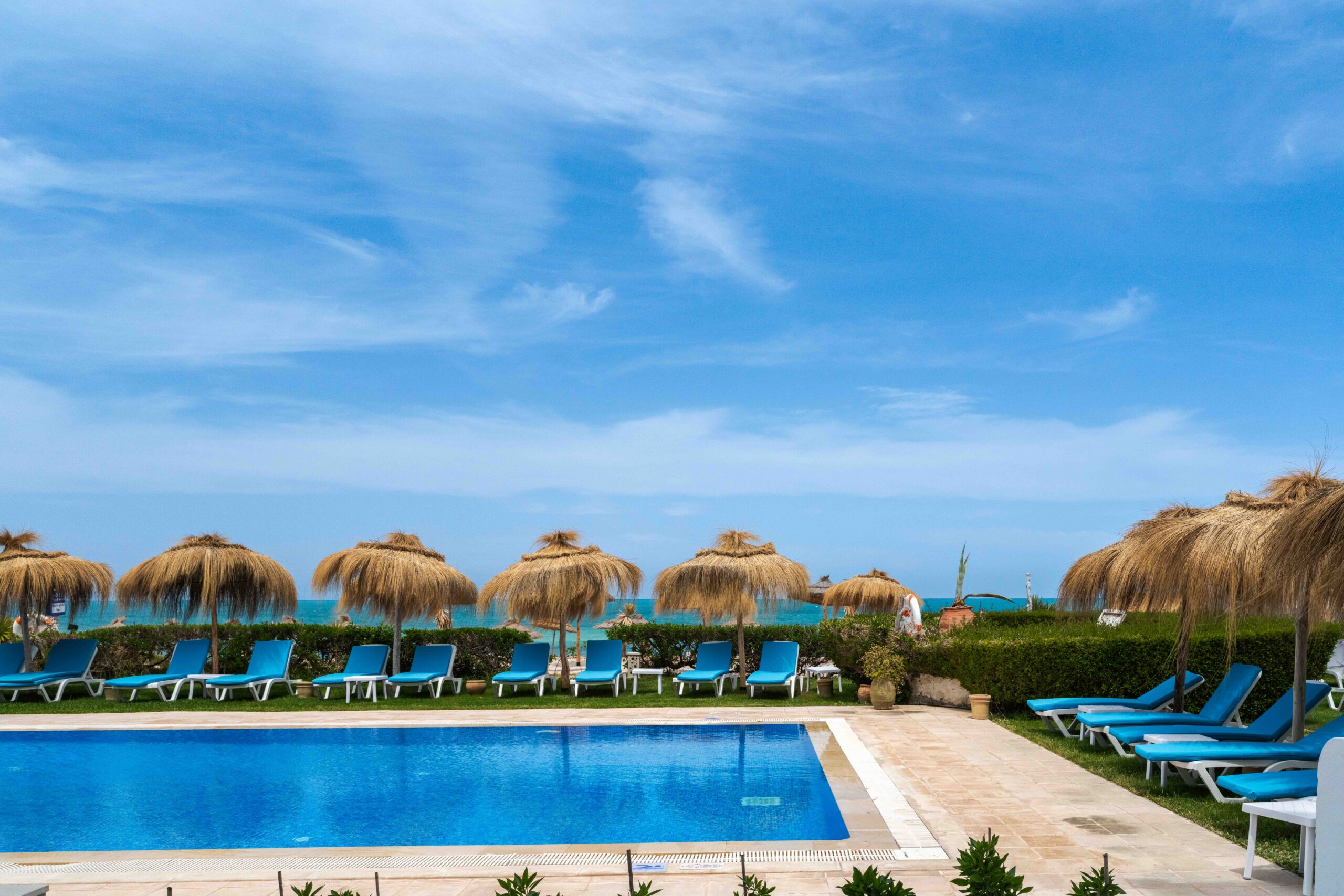 Piscine bordée de parasols en paille face à la mer Méditerranée
